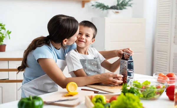 Bağlanma kavramı. Neşeli anne oğluna yemek pişirmede yardım ediyor, küçük çocuğa sağlıklı sebze salatası yapmayı öğretiyor, havuç rendeliyor, evde birlikte yemek pişiriyor..