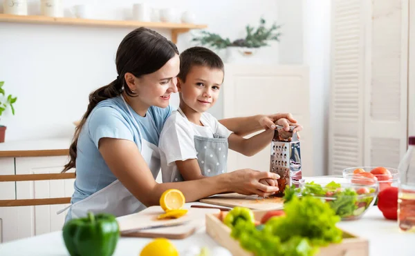 Bağlanma kavramı. Neşeli anne oğluna yemek pişirmede yardım ediyor, küçük çocuğa sağlıklı sebze salatası yapmayı öğretiyor, havuç rendeliyor, evde birlikte yemek pişiriyor..