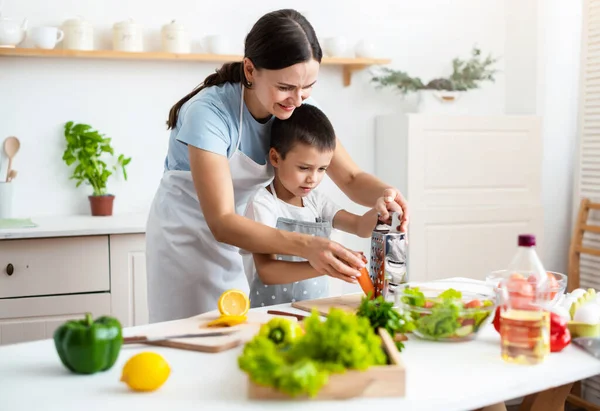 Bağlanma kavramı. Neşeli anne oğluna yemek pişirmede yardım ediyor, küçük çocuğa sağlıklı sebze salatası yapmayı öğretiyor, havuç rendeliyor, evde birlikte yemek pişiriyor..