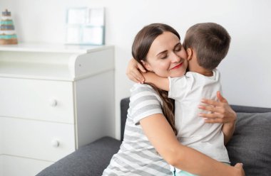 Küçük anaokulu çocuğu, mutlu anneye sarılıp tahta masa oyunu oynuyor, evde güzel vakit geçiriyor..