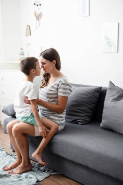 Küçük anaokulu çocuğu, mutlu anneye sarılıp tahta masa oyunu oynuyor, evde güzel vakit geçiriyor..