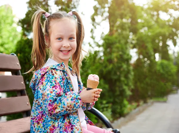 在户外的长椅上坐着一个笑容满面的小女孩 她带着乳酪蛋卷里的冰淇淋 假期和夏季时间概念 — 图库照片