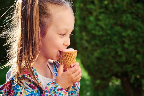 Cheerful kid girl with ice cream in waffle cone is eating licking tongue ice cream. Close-up ice cream. Summer dessert for kid and summer time concept