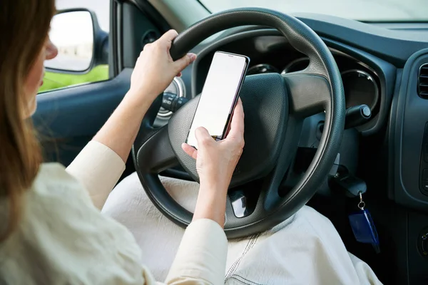 Araba sürerken cep telefonu kullanmak yok. Cep telefonu tutan kadın sürücü yeni bir arabada direksiyon simidi tutuyor. Seçici odak, kırpılmış.