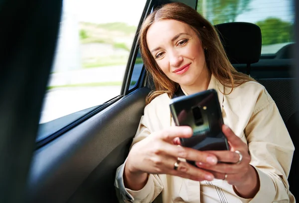 Schöne Geschäftsfrau Benutzt Ein Smartphone Und Lächelt Auf Der Rückbank Stockbild