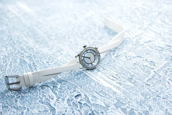 Жіночі годинники з білим ремінцем лежать на сірому фоні . Стокове Зображення