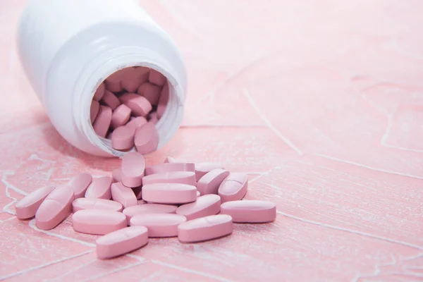 Rózsaszín pirulák rózsaszín háttérrel. Tabletta fehér üvegben — Stock Fotó