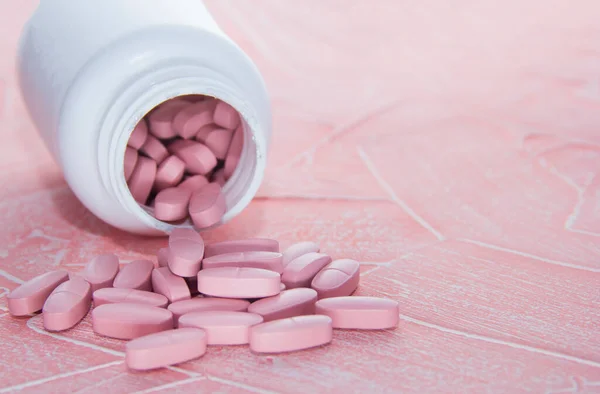 Rózsaszín pirulák rózsaszín háttérrel. Tabletta fehér üvegben — Stock Fotó