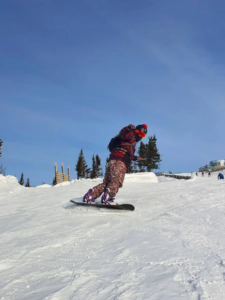 Un hombre está haciendo snowboard. Un snowboarder macho activo, montando cuesta abajo, snowboard de cerca. Foto vertical — Foto de Stock