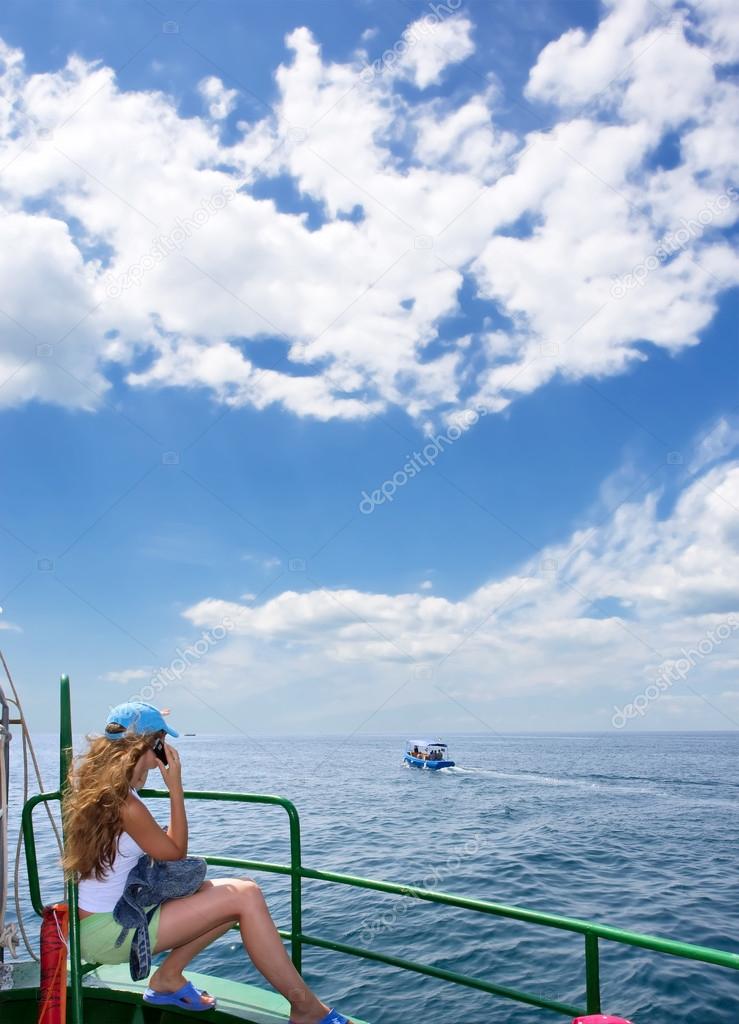 Blonde girl calls on phone while sitting on boat's desk