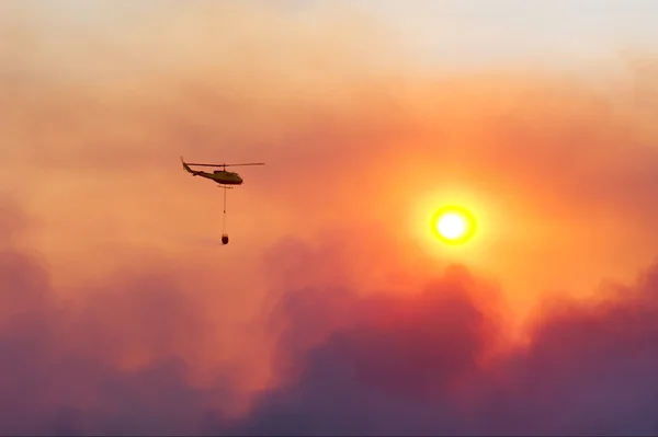 Bombeiros resgate helicóptero amortecimento fogo contra o pôr do sol — Fotografia de Stock