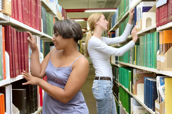 Two friendly girls, European and African, between bookshelves — 图库照片