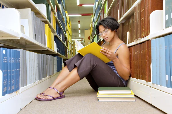 Afrikansk tjej läser bok satt på biblioteket våningen — Stockfoto