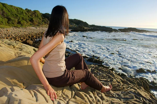 Giovane ragazza si siede su rocce e guarda il mare — Foto Stock