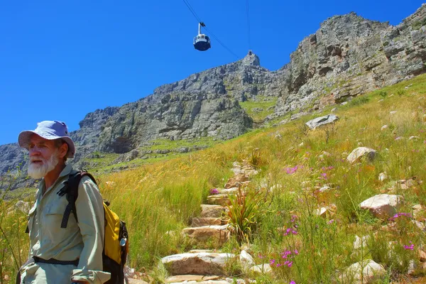 Old man walks down the trail under cable car — Stock Photo, Image