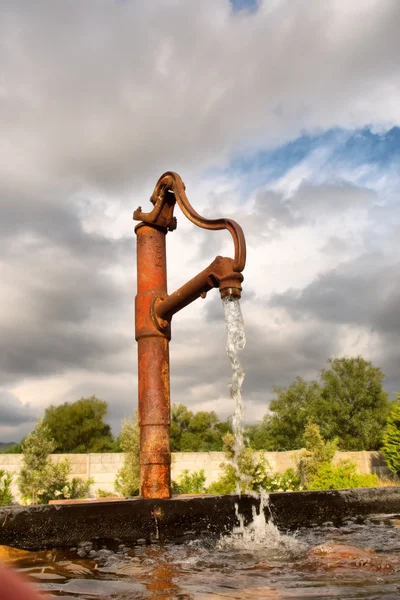 Rubinetto d'acqua arrugginito alla luce del tramonto contro cieli drammatici — Foto Stock