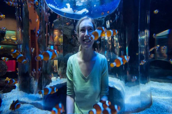 Mujer feliz mira peces payaso a través de vidrio — Foto de Stock