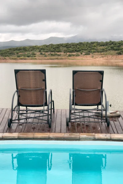 Two chairs between swimming pool and lake in mountains — Stock Photo, Image