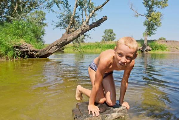Glücklicher nasser Junge klettert auf Felsen im See — Stockfoto