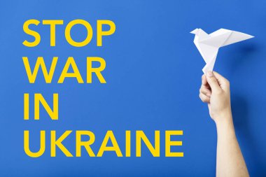 Ukrayna 'daki savaşı mavi arka planda sarı harflerle durdurun, Ukrayna bayrağının renkleri, beyaz kağıt güvercin tutan bir elin yanında, barışın sembolü..