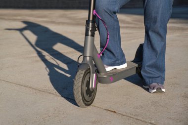 Güneşli bir sabahta şehirde elektrikli scooterıyla tanınmayan bir kadın. Sürdürülebilirlik kavramları, modern ve aktif yaşam, temiz enerji ve yeşil hareketlilik, ekolojik ulaşım.