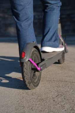 Yakın çekim görüntüsü, şehrin güneşli bir sabahında elektrikli scooterlı kadın bacakları. Sürdürülebilirlik, modernlik, temiz enerji ve yeşil hareketlilik kavramları, ekolojik ulaşım.