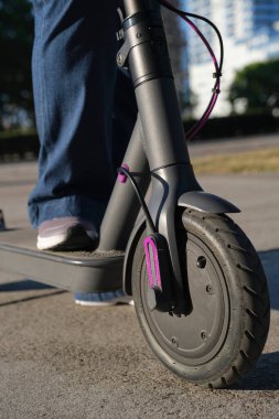 Yakın çekim görüntüsü, şehrin güneşli bir sabahında elektrikli scooterlı kadın bacakları. Sürdürülebilirlik, modernlik, temiz enerji ve yeşil hareketlilik kavramları, ekolojik ulaşım.