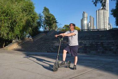 Güneşli bir sabahta şehirde elektrikli scooterı olan İspanyol bir son sınıf öğrencisi. Sürdürülebilirlik, modernlik, aktif yaşam, temiz enerji ve yeşil hareketlilik kavramları, ekolojik ulaşım.