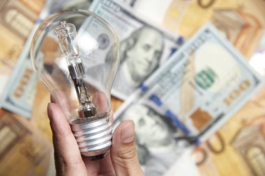 Banknotların arka planında ampul tutan bir kadın. Enerji verimliliği, elektrik pahalı maliyet ve güç tüketimi kavramları.