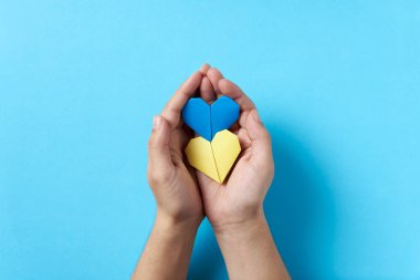 Ukrayna bayrağının mavi ve sarı renkli bir çift kağıt kalbi tutan ve koruyan bilinmeyen birinin elleri. Rus askeri işgali sırasında Ukrayna 'yı destekleyen sembolik imaj.