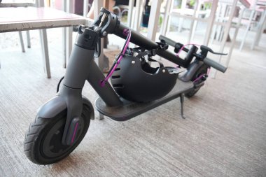 Katlanmış elektrikli scooter 'lar açık hava restoranındaki bir masanın yanına yerleştirilmiş spor kaskları. Kentsel yaşam için pratik ve çevre dostu ulaşım sistemi.