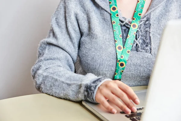 Unrecognizable person studies or works at home with a laptop using a sunflower lanyard, symbol of people with invisible or hidden disabilities.