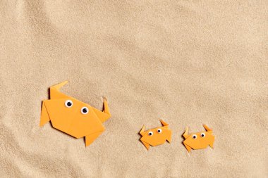Eğlenceli bir yaz manzarası tasarımı, plaj ve tatil kavramları: dost canlısı bir origami ailesi olan pürüzsüz kum arka planı. Yaratıcı düzen, çocuklar için kopyalama alanı ile minimal bileşim.