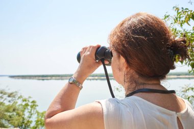 İspanyol olgun kadın, Arjantin, Entre Rios 'taki El Palmar Ulusal Parkı' ndaki bir gözcü noktasından dürbünden bakıyor. Konseptler: aktif yaşam, doğaya seyahat, açık hava ve maceranın tadını çıkar