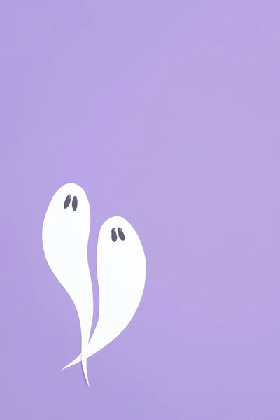 Cute minimal halloween composition, couple of white ghosts flying on lilac background, pastel color design with copy space.