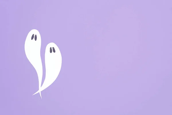 Cute minimal halloween composition, couple of white ghosts flying on lilac background, pastel color design with copy space.