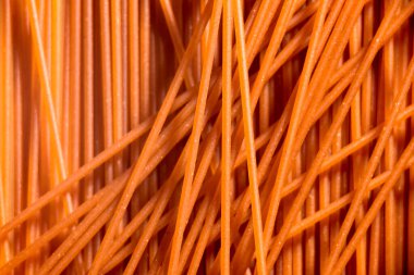 Italian healthy food background, raw red sweet bell pepper spaghetti in a textured design of uncooked pasta lines.