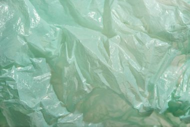 Green plastic background, wrinkled single use bag. Concepts: sustainability, recycling, pollution.