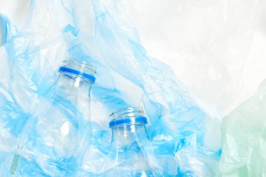 Plastic transparent disposable bottles over, green and blue wrinkled single use plastic bags. Concepts: sustainability, recycling, pollution.