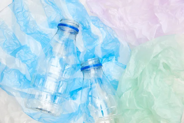 Plastic transparent disposable bottles over lilac, green and blue wrinkled single use plastic bags. Concepts: sustainability, recycling, pollution.