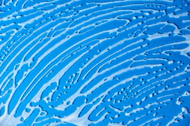 Top view of a blue glass surface covered with soap foam. Monochromatic background without people, concept of cleanliness.