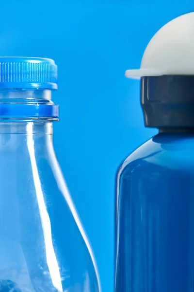 Pair of bottles, a plastic transparent disposable one and a blue metal reusable one. Concepts: sustainability, recycling, reusing, pollution, zero waste campaigns.