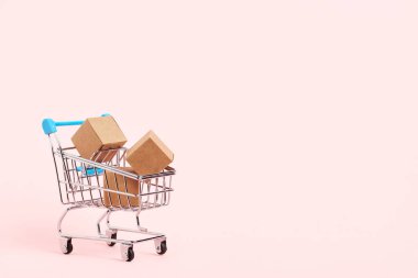 Shopping cart with cardboard boxes on a pastel pink background. Bright minimalist design with copy space. Concepts: market sales, seasonal discounts, logistics, packaging.
