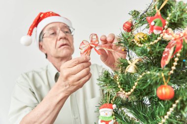 Kıdemli İspanyol süslemeci, kırmızı Noel Baba şapkası takmış kırmızı kurdele takıyor..