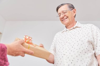 Kıdemli Latin çift tatillerini mutlu bir şekilde evde geçiriyorlar. Bilinmeyen bir kadının elleri ona bir Noel hediyesi veriyor ve ona gülümsüyor. Kopya alanı ile düşük açı görünümü bileşimi.