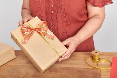 Tarafsız kağıt ve geleneksel kordon ve kurdelelerle Noel hediyelerini paketleyen tanınmayacak kadar olgun bir kadın. Kopyalama alanı olan parlak tasarım.