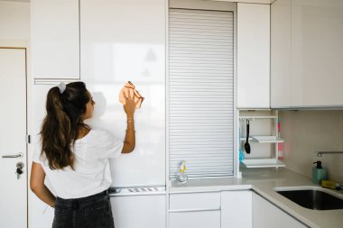 young woman cleaning white and bright kitchen