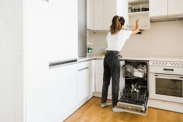 Young woman putting away clean dishes in kitchen — 스톡 사진