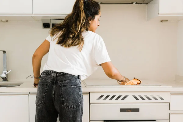 Junge Frau putzt Keramikherd in Küche — Stockfoto