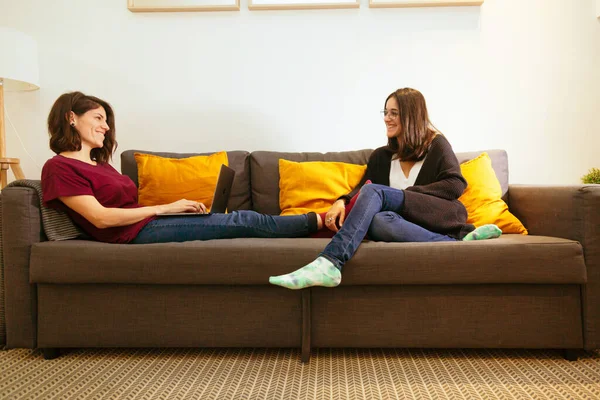 Coppia lesbica guardando a vicenda e ridendo sul divano con il computer portatile — Foto Stock
